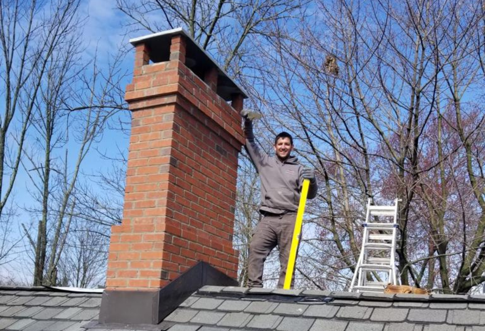Lasting Construction team member posing next to a brick chimney he just built.